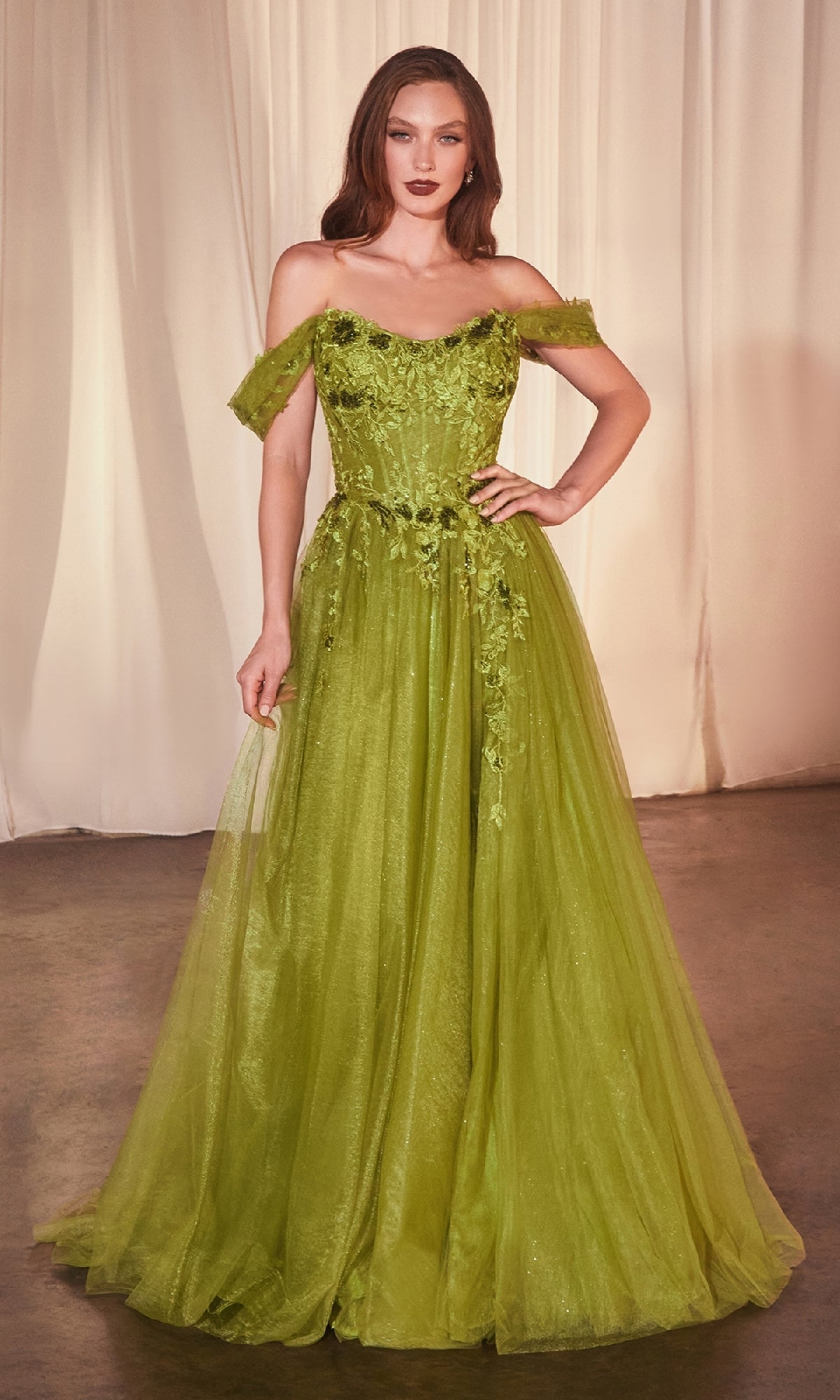 A woman stands before beige curtains wearing the Ladivine CD799 Off-Shoulder Long Prom Dress—a green, floor-length evening gown with floral embellishments and a tulle skirt.